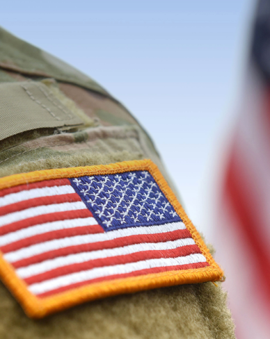 American flag patch on a military uniform with a blurred flag in the background