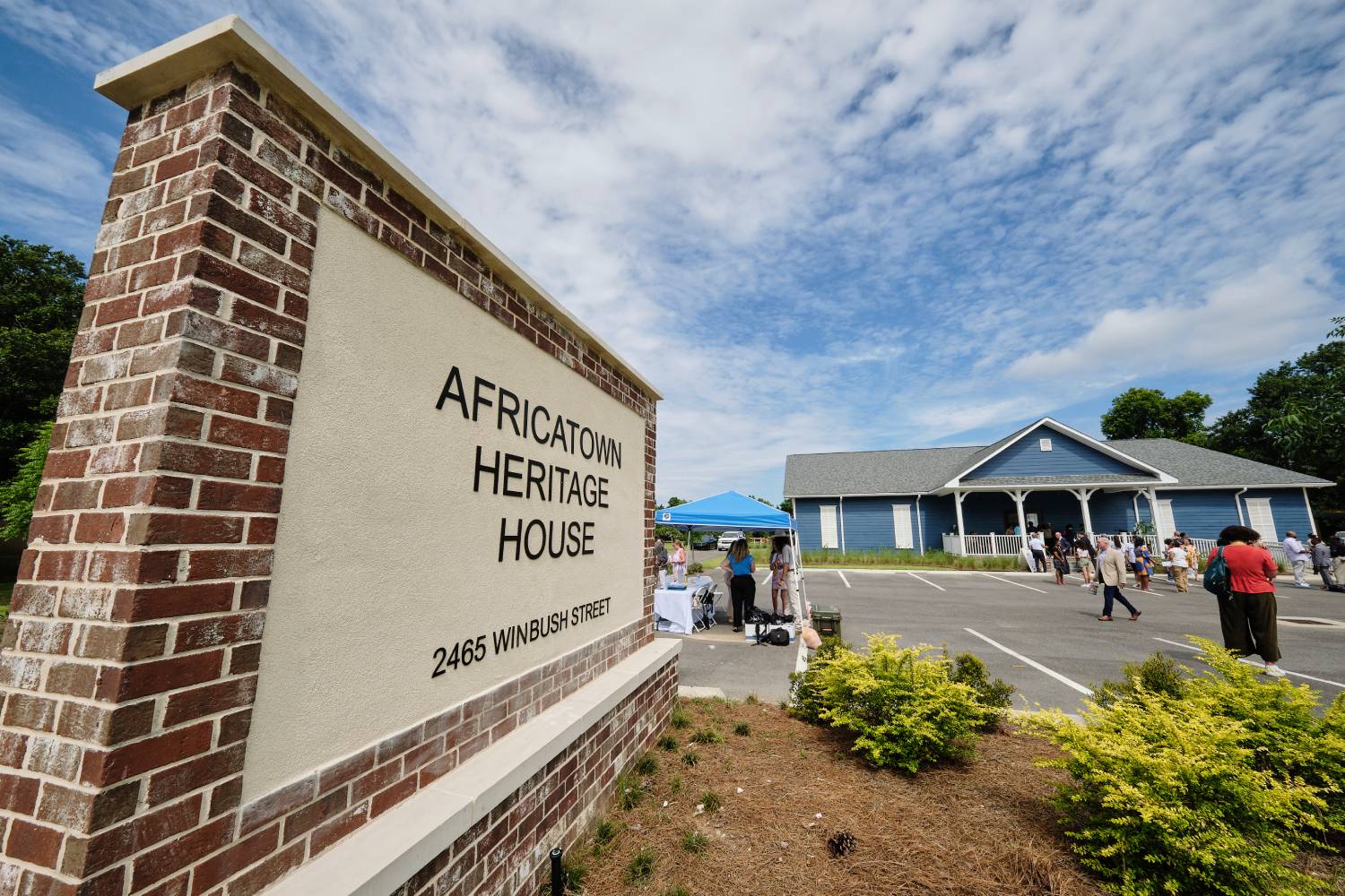 Sign for Africatown Heritage House with visitors gathered outside the museum building under a blue sky