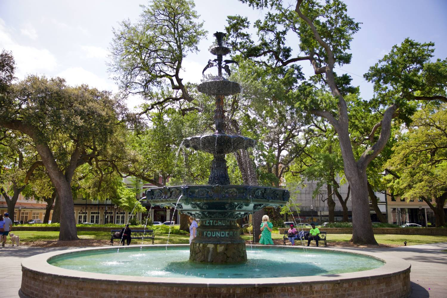Historic fountain in a shaded city park surrounded by mature oak trees and visitors enjoying the square