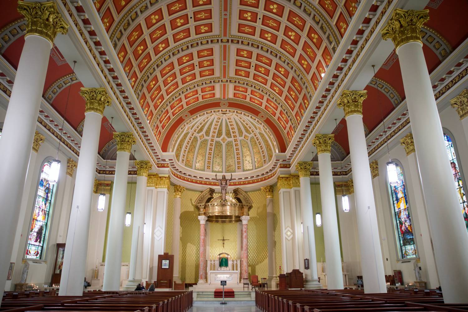 Interior of a historic church featuring a vaulted ceiling, stained glass windows, and an ornate altar framed by tall columns