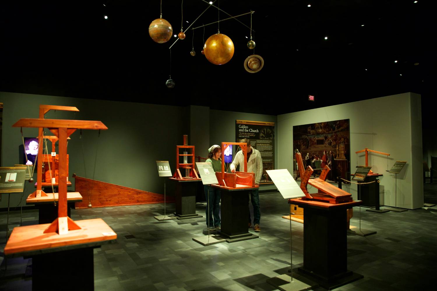 Visitors viewing historical science exhibits and astronomical models inside a museum gallery.