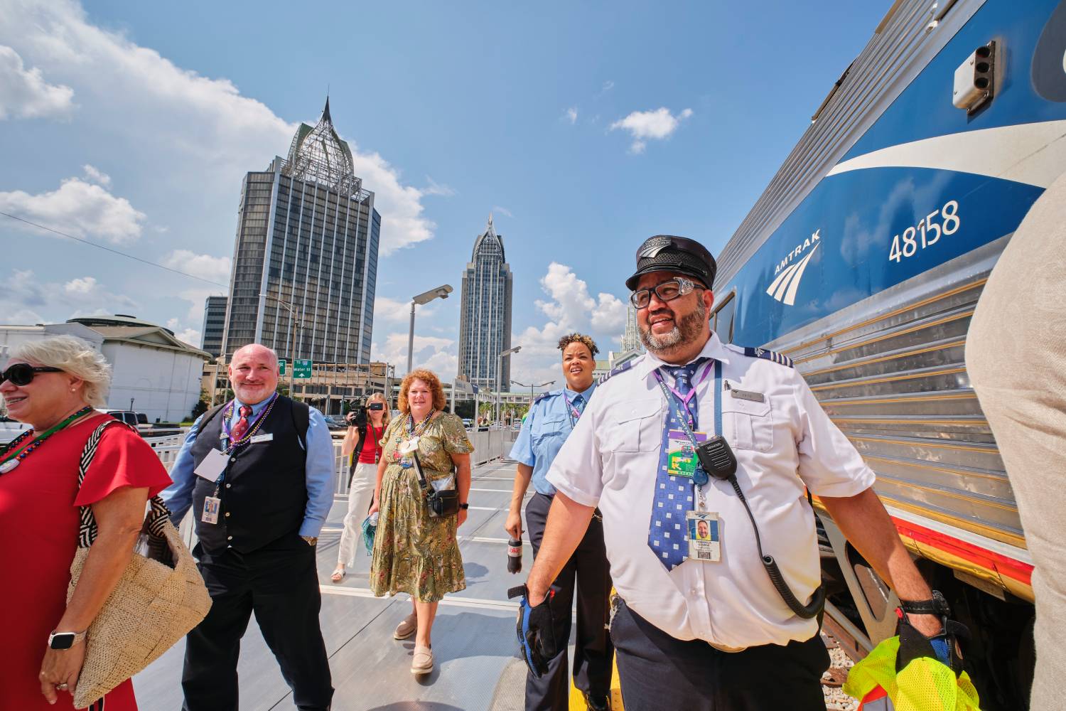 Amtrak crew members and passengers walking beside a train at Mobile station with the downtown skyline in the background.